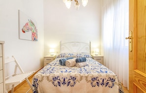A neatly made bed with a patterned bedspread, two bedside lamps, a wall-mounted artwork, and a wooden door. - Gorgeous apartment in San Javier (San Javier)