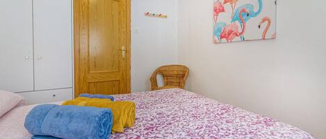 Ein Schlafzimmer mit einem Bett, einer Holztür, einem Korbstuhl und einer Wand mit einem Flamingo-Gemälde.