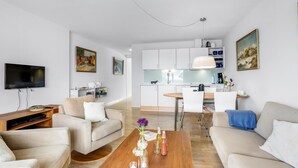 A modern living room with a TV, sofa, coffee table, and a view into the kitchen. - Cozy apartment in Gudhjem (Gudhjem)