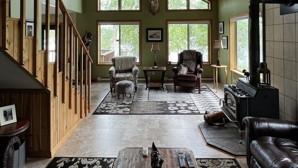 Ein geräumiges Wohnzimmer mit hoher Decke, Holzbalken, Kamin und großen Fenstern.