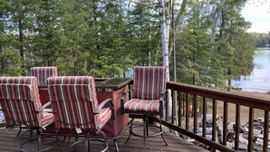 Eine Terrasse mit vier gestreiften Stühlen und einem Tisch, mit Blick auf einen Fluss und ein bewaldetes Gebiet.