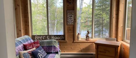 A cozy cabin interior with a plaid sofa, a wooden desk, and large windows overlooking a forest.