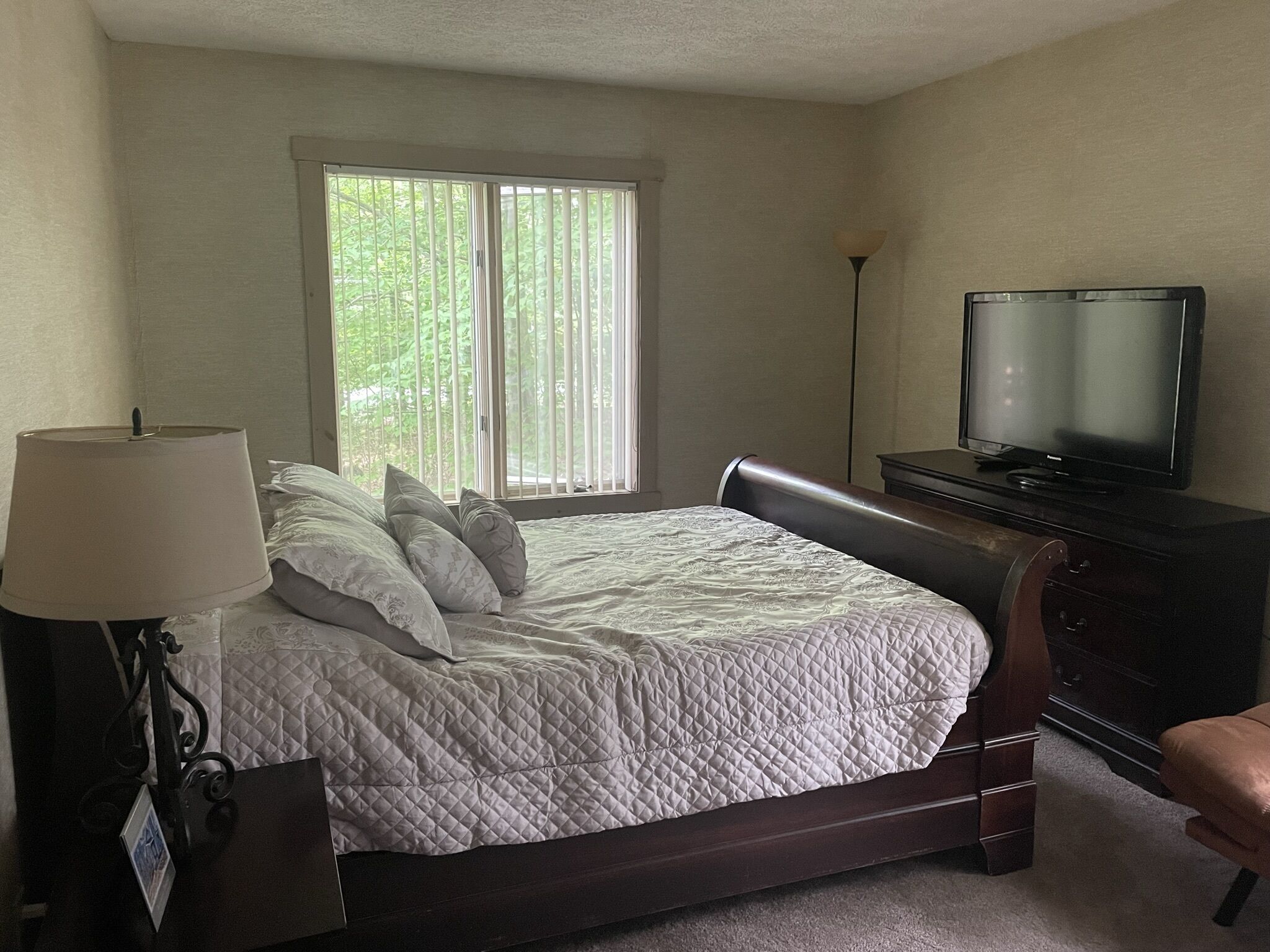 Un dormitorio con cama, televisión, lámpara y ventana con persianas.