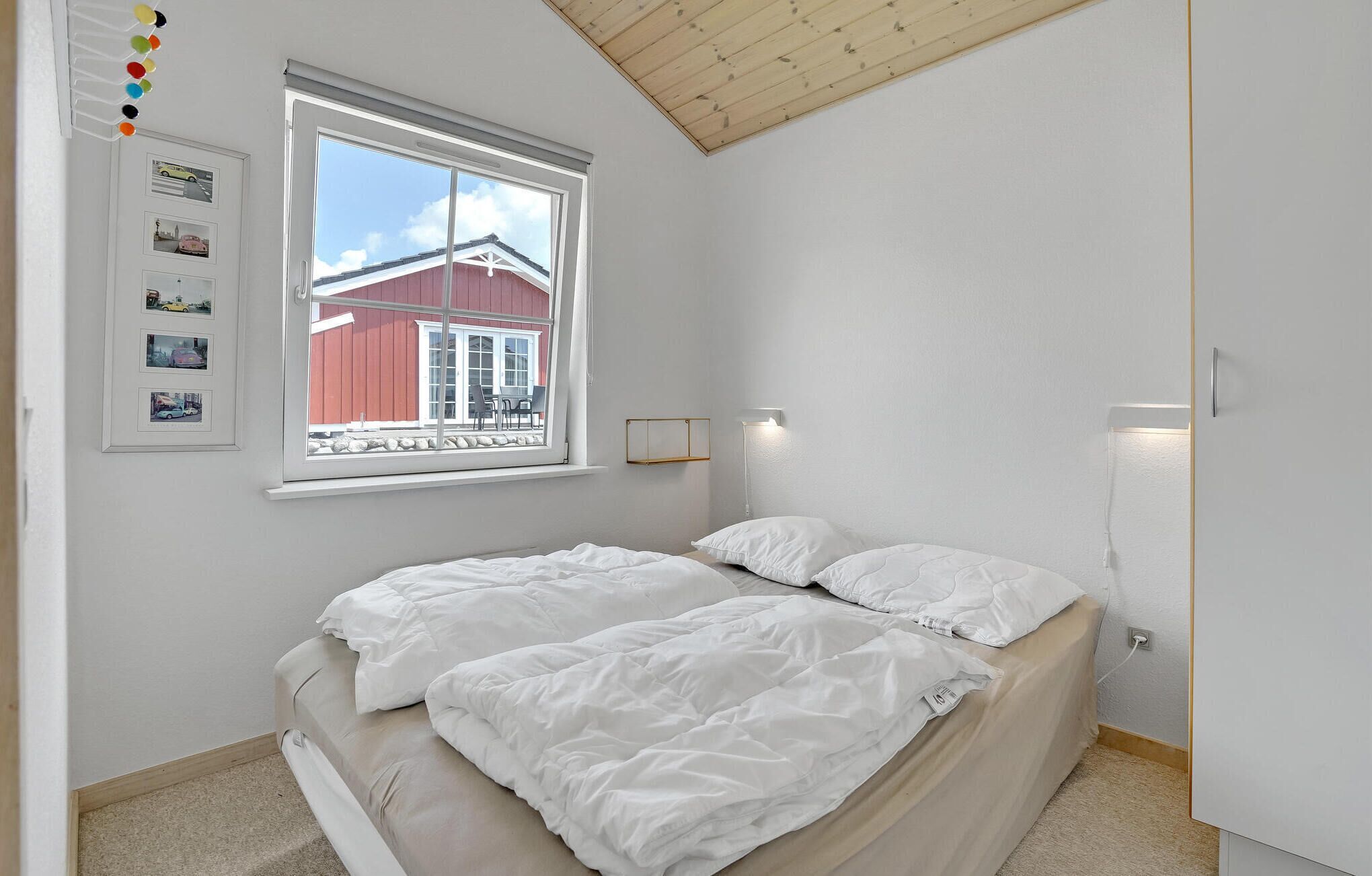 Ein Schlafzimmer mit einem Bett, einem Fenster mit Blick auf ein rotes Gebäude und einem an der Wand befestigten Bilderrahmen mit Fotos.