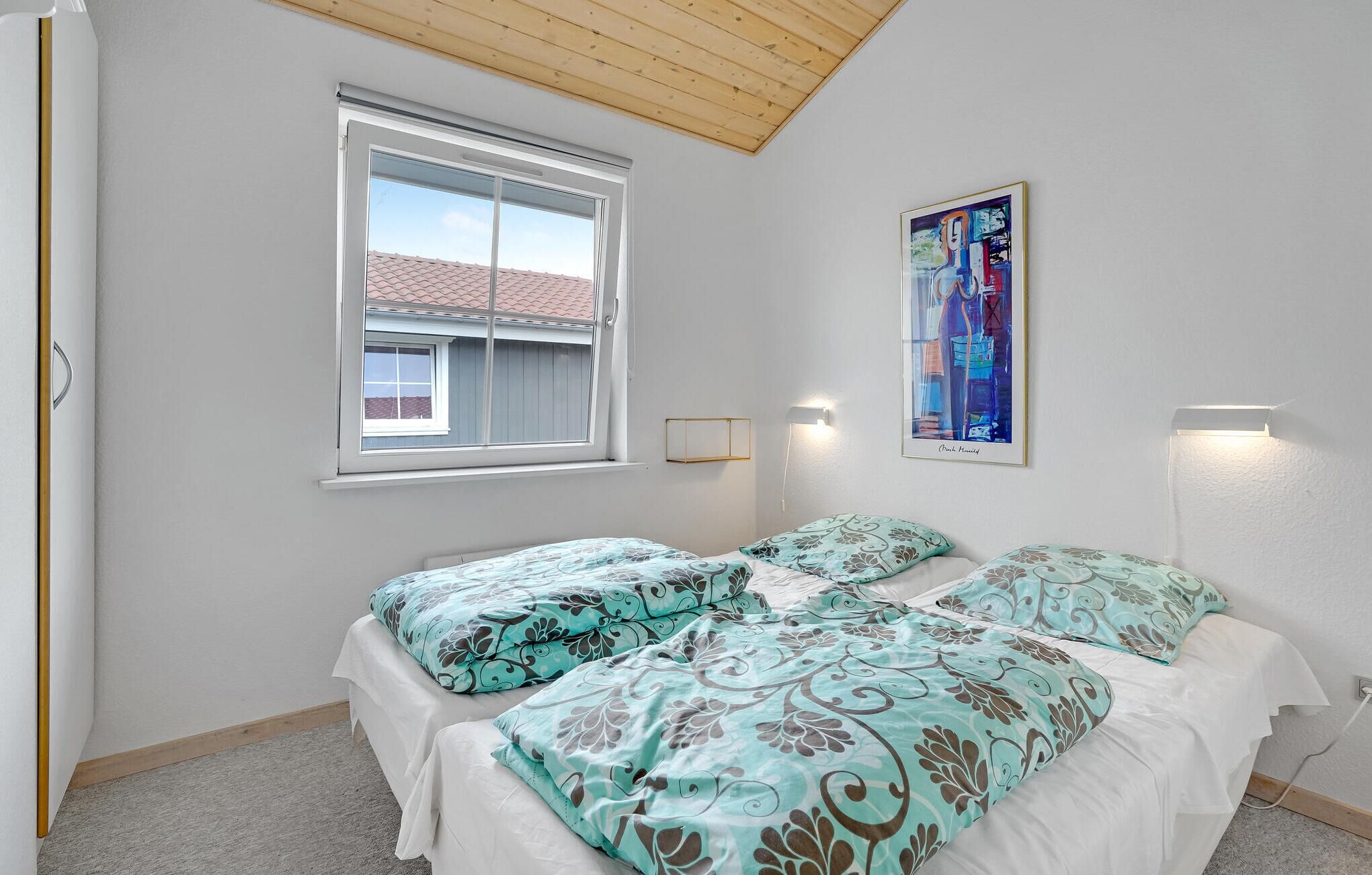 Quarto com duas camas, uma janela, uma luminária no teto e um quadro na parede.