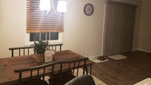 A dining area with a wooden table, chairs, a potted plant, a candle, and a clock on the wall. - Comfortable 3 Bedroom, 3 Bathroom With Amenities! (Savannah)