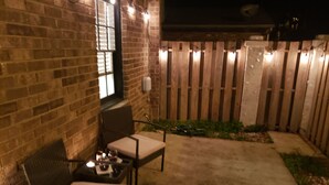 A patio area with brick walls, a wooden fence, and outdoor furniture including two chairs and a table. - Comfortable 3 Bedroom, 3 Bathroom With Amenities! (Savannah)