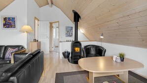A cozy loft-style living room with a high ceiling, a black wood-burning stove, a leather sofa, a dining table, and a view of the adjacent kitchen. - Nice home in Gråsten with WiFi (Gråsten)