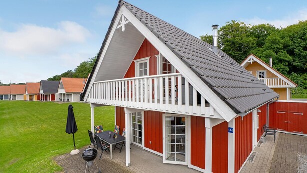 A red and white building with a balcony, a grill, and a table with chairs. - Nice home in Gråsten with WiFi (Gråsten)