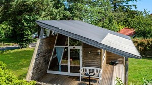 Une petite cabane en bois avec un toit en pente, une porte d’entrée en verre et une terrasse dotée d’une table et d’un banc.