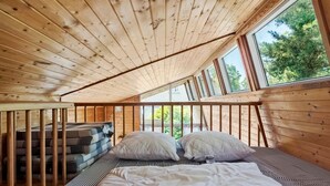 Une chambre confortable située sous les toits, avec un plafond en pente, des poutres en bois et de grandes fenêtres donnant sur un paysage verdoyant.