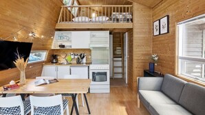 Un intérieur de chalet chaleureux comprenant un coin repas, une cuisine, une chambre en mezzanine et un canapé.