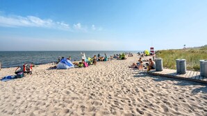 Une plage de sable où l’on peut voir des gens bronzer et se baigner, ainsi que des tentes et des chaises de plage.