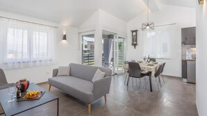 A modern living room with a grey sofa, dining table with chairs, and a kitchen area with a stove and cabinets. - 2 bedroom nice apartment in Vrbnik (Vrbnik)