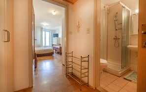 A hotel room with a bed, a bedside table, a shower area, and a bathroom.