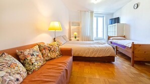 Une pièce comprenant un canapé, deux lits, une lampe, un téléviseur et une fenêtre.