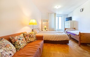 A room with a sofa, two beds, a lamp, a TV, and a window. - Beautiful apartment in Portoroz (Portoroz)