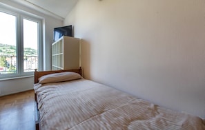 A single bed with a wooden frame and a striped bedspread in a room with white walls and a large window.