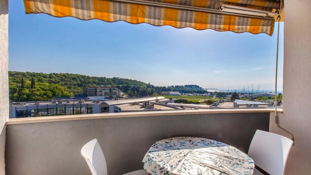 Un balcon avec une table et des chaises, donnant sur un paysage urbain avec des bâtiments et de la verdure.