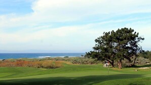 Ein Golfplatz mit Blick auf das Meer und Berge im Hintergrund.