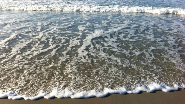 Ein sandiger Strand mit sanften Wellen, die an das Ufer schlagen.