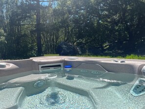 Un jacuzzi con ventilación integrada y portavasos, rodeado de vegetación boscosa.
