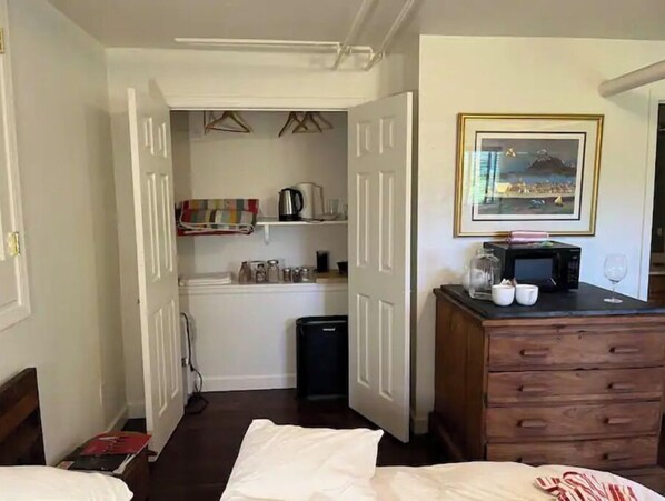 Hotelkamer met een bed, een dressoir, een magnetron en een kleine kitchenette met een waterkoker en potjes.