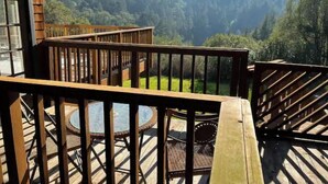 A wooden deck with a glass table and chairs, overlooking a forested valley. - Unique private access studio with outdoor spa in paradise. (Nicasio)