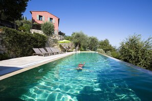 Une piscine à l’eau claire, entourée de chaises longues et d’un mur en pierre.