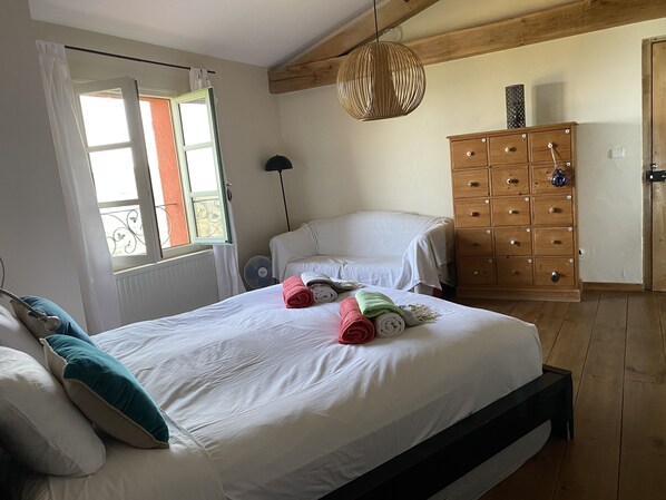 Une chambre à coucher avec un grand lit, une commode en bois, un luminaire suspendu et une fenêtre avec des rideaux.