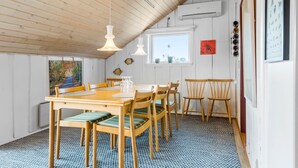 Een eetruimte met een houten tafel en stoelen, een raam met uitzicht, en een wandairconditioning.