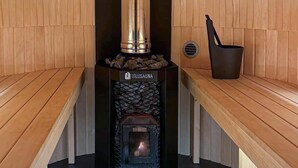 A wood-burning stove with a metal chimney, a metal bucket, and a wooden bench.