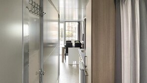 A hallway with a modern design, featuring a glass door with a metal handle, a wooden floor, and a view of a balcony with a table and chairs.