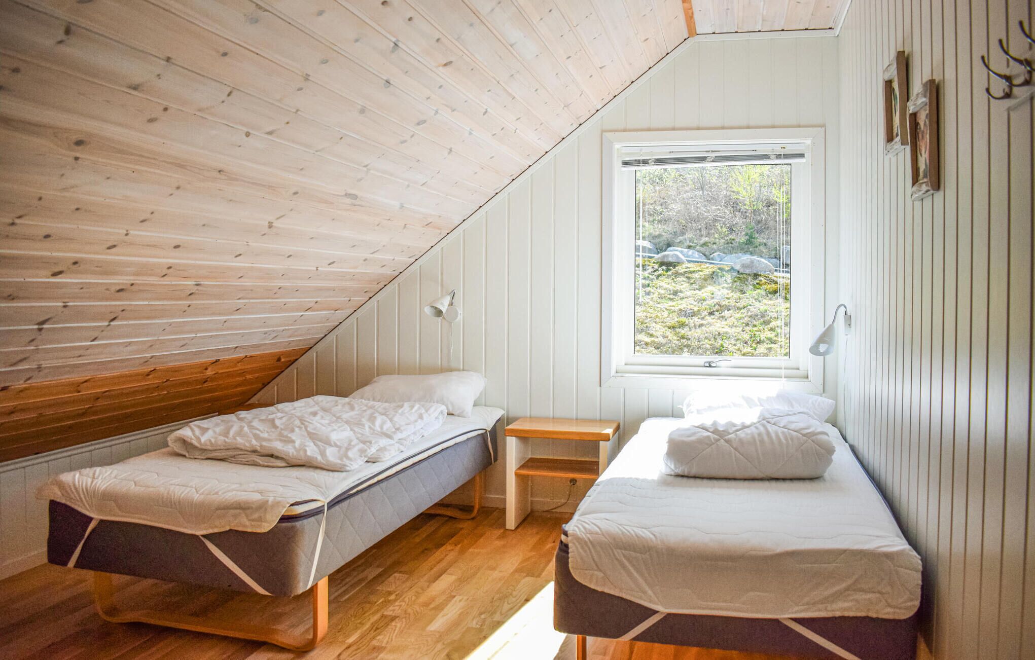 A small, cozy attic bedroom with two single beds, a wooden floor, and a window offering a view of a rocky landscape.