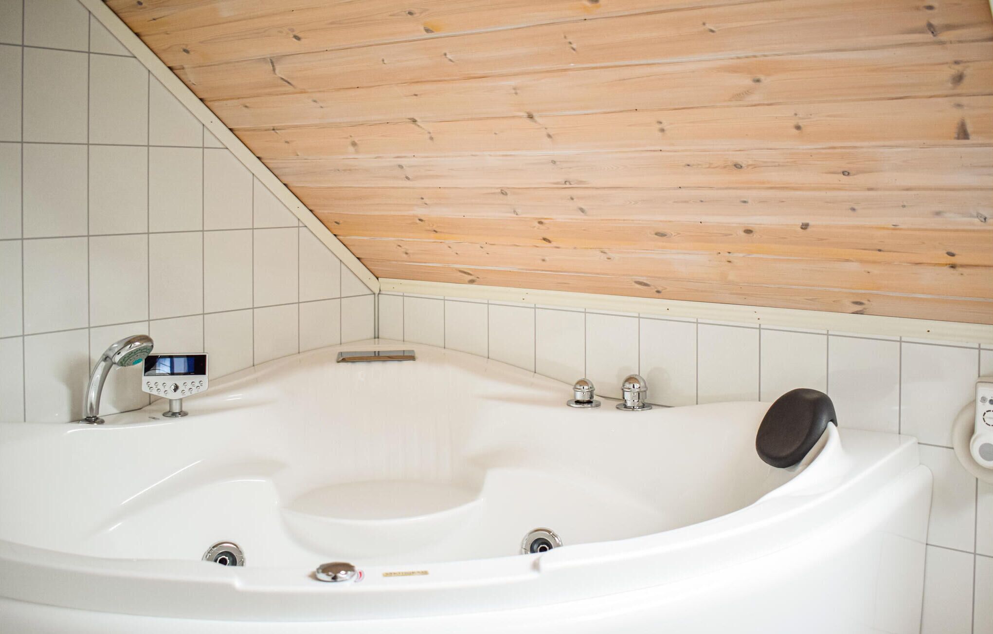 A modern bathroom with a freestanding bathtub, wooden ceiling, and white tiled walls.