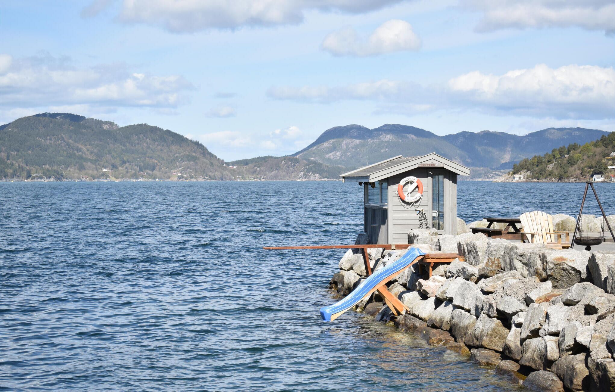 A lifeguard station with a lifebuoy, a wooden chair, and a swing chair by a rocky shore.