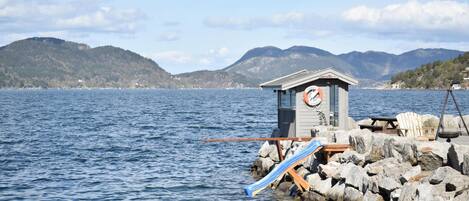 A lifeguard station with a lifebuoy, a wooden chair, and a swing chair by a rocky shore.