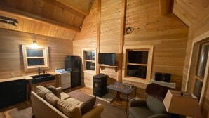Un interior acogedor de cabaña de madera con cocina, dos sofás, una mesa y una chimenea.