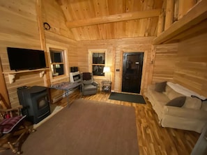 A cozy log cabin interior with a fireplace, sofa, and television.
