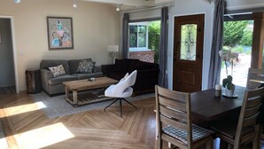 A spacious living room with a wooden herringbone floor, a grey sofa, a wooden coffee table, and a dining area with a wooden table and chairs. - Beautiful, private, sunny, ideal location, 31 night minimum (Carmel Valley)