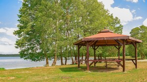 A gazebo with a roof and benches, surrounded by trees and a body of water.