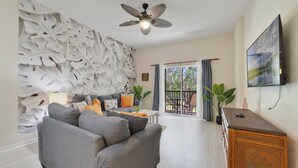 Una sala de estar moderna con un sofá gris, un aparador de madera, un ventilador de techo y un televisor grande en la pared.