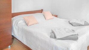Una cama bien hecha con una colcha blanca acolchada, dos almohadas rosas y dos toallas blancas dobladas.