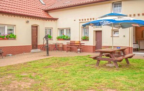 Relax on the patio with a wooden table and benches, shaded by a blue umbrella.