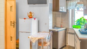 Cocina compacta con refrigerador, pileta, mesa con silla y ventana con vista a vegetación.