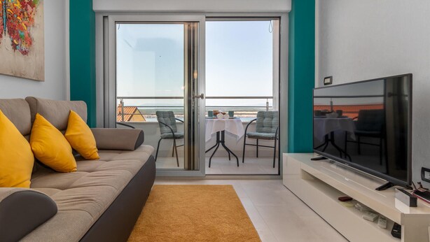 Un salon moderne avec un canapé, un téléviseur et un balcon équipé d’une table et de chaises.