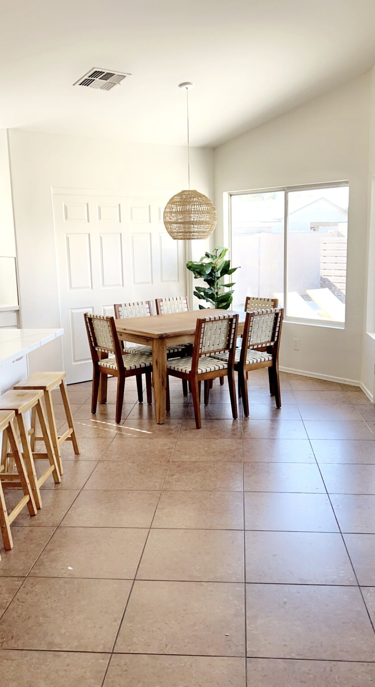 A dining area with a wooden table and chairs, a hanging light fixture, and a large window.