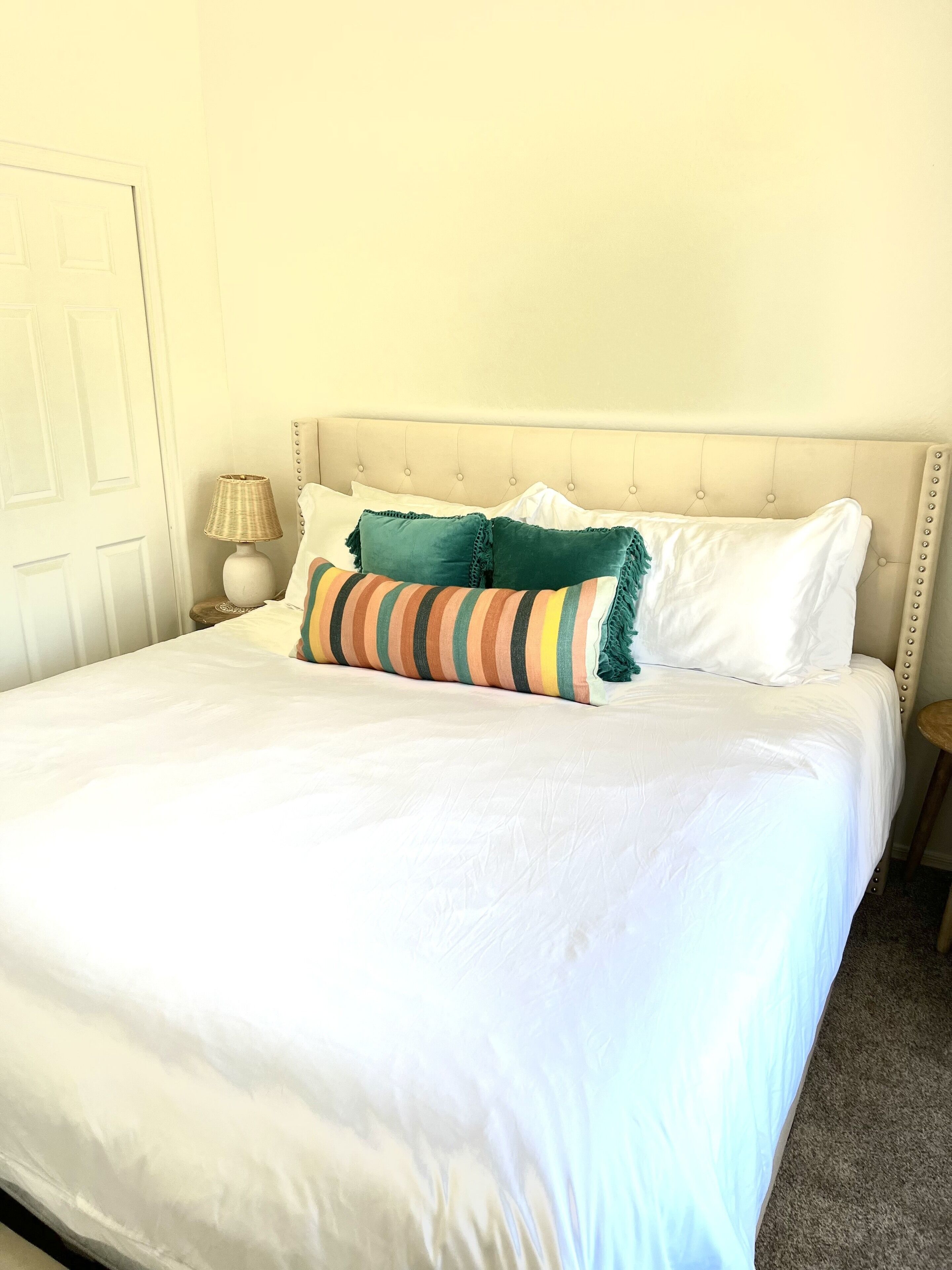 A neatly made bed with white linens, a striped pillow, and two solid-colored pillows.