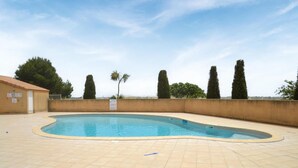 Una piscina con bordo piastrellato, circondata da un muretto e alberi.