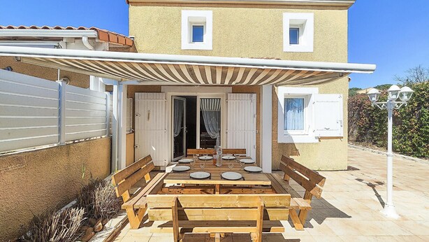 Una casa con un portico coperto, panchine in legno e un tavolo da pranzo per quattro persone.